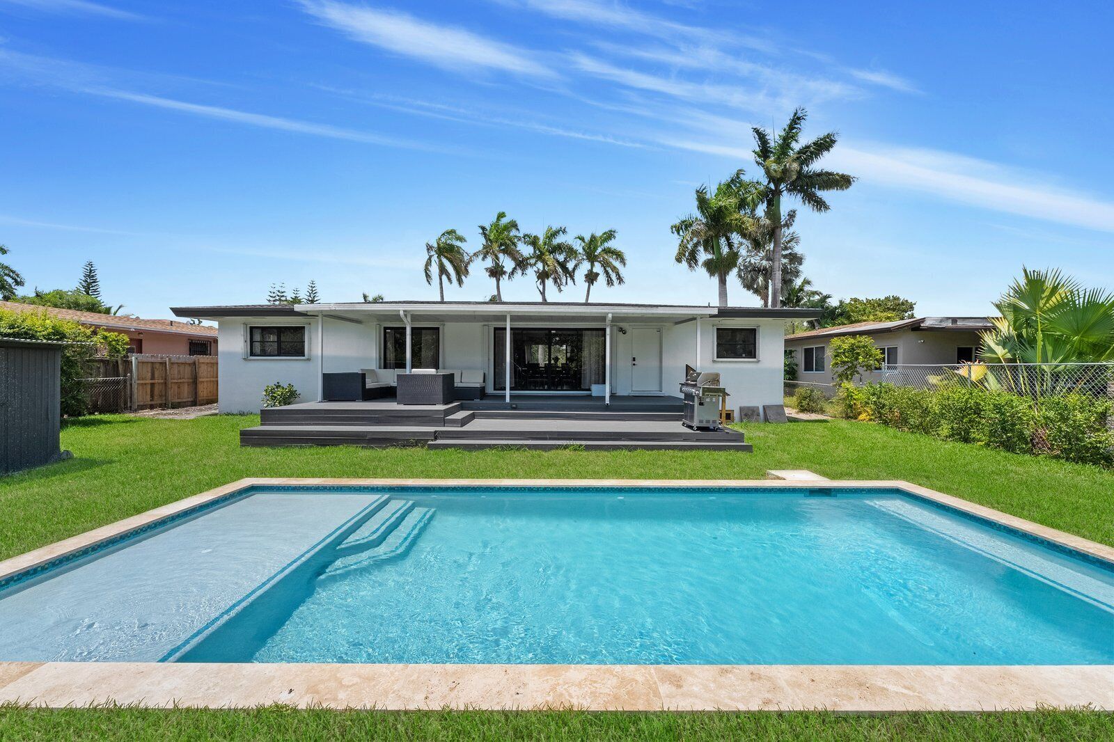 Une maison moderne dotée d’une piscine, d’un patio couvert et de palmiers.