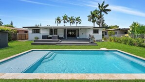 Ein modernes Haus mit Swimmingpool, überdachter Terrasse und Palmen.