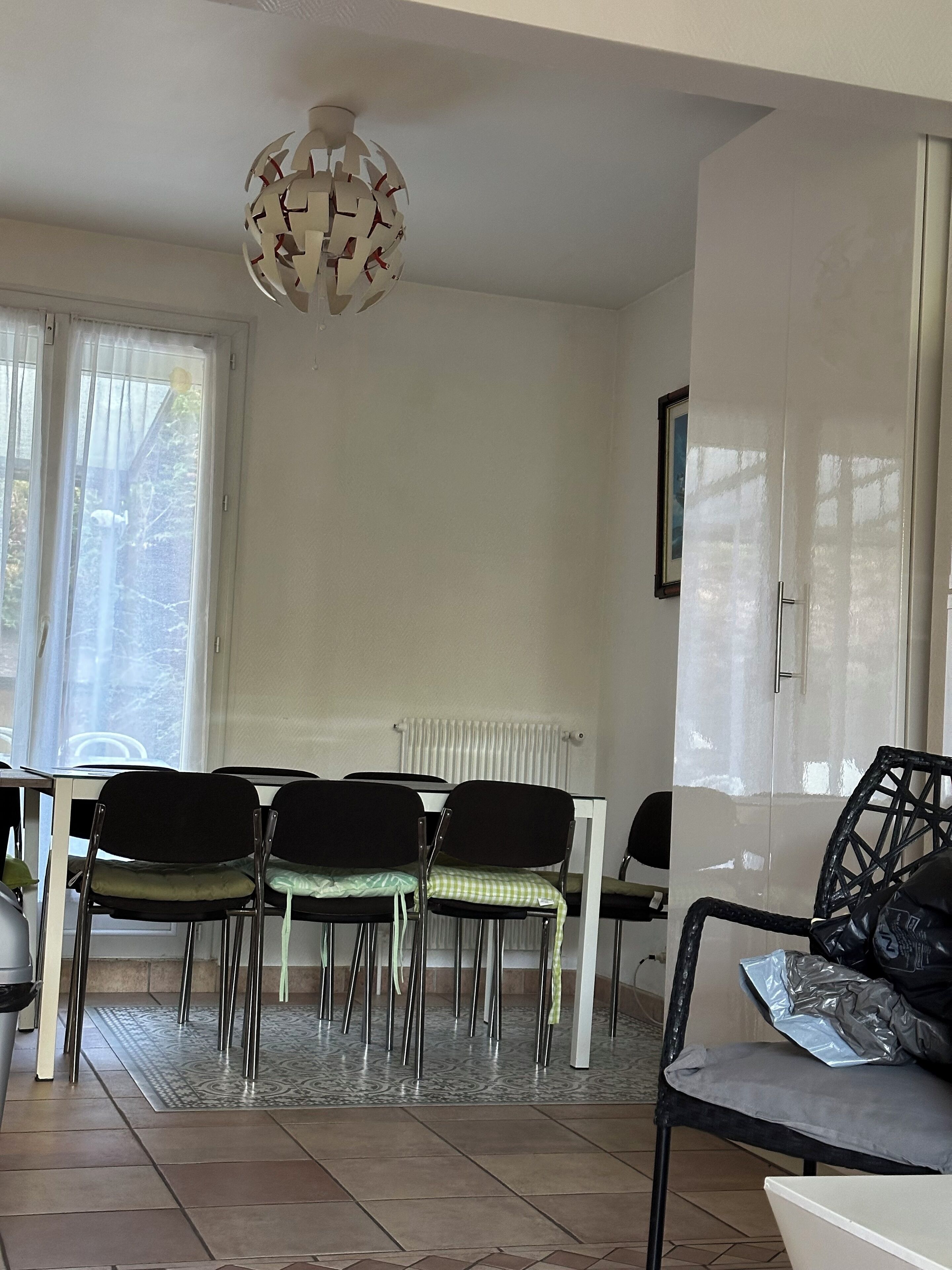 A dining area with a white table, four black chairs, a patterned rug, and a ceiling light fixture.