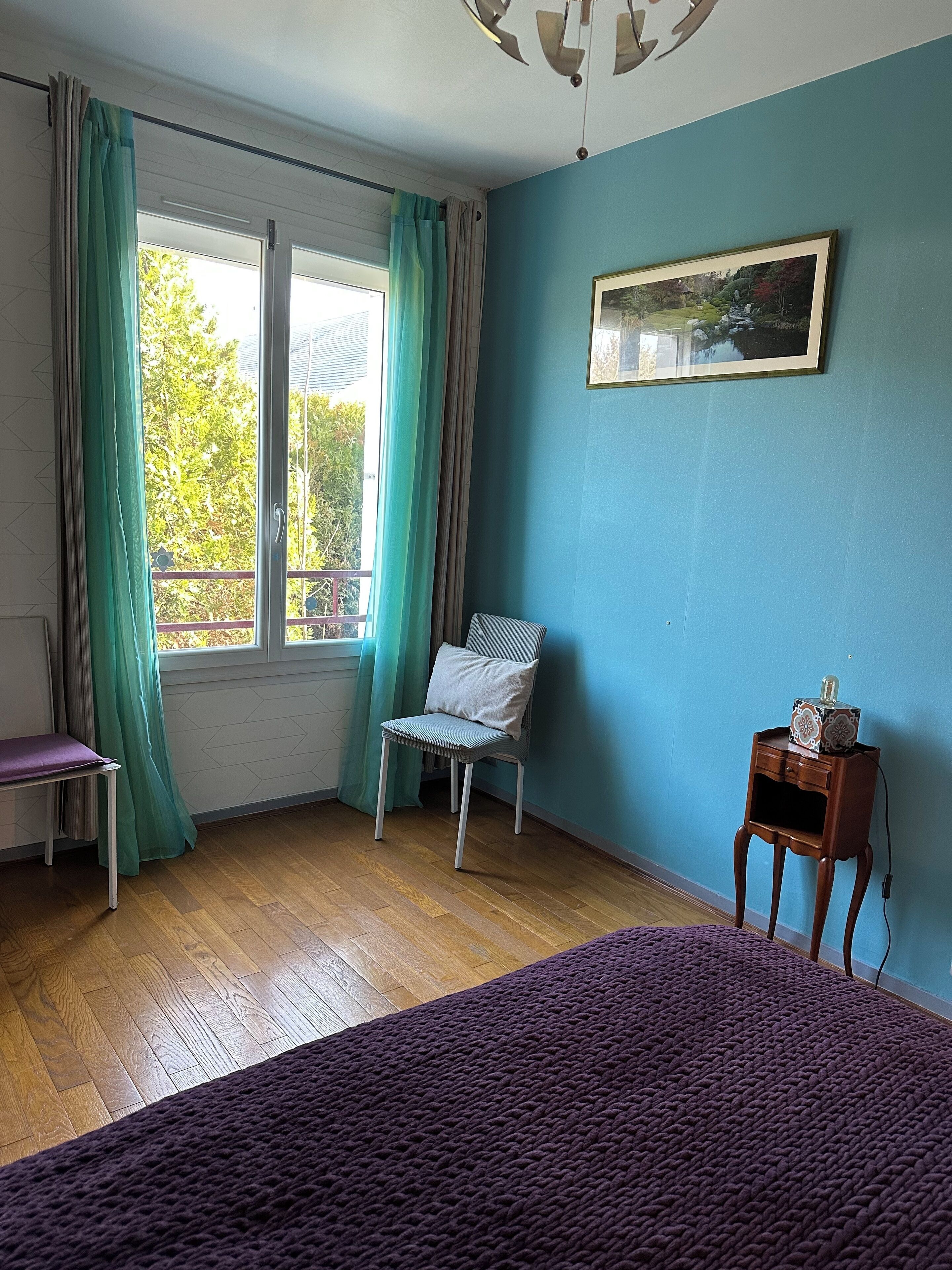 Een kamer met een bed, een stoel, een tafeltje en een raam met gordijnen.