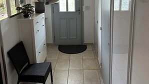 A hallway with a door, a chair, a small table with a plant, and a window with a curtain.