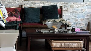 A cozy living room with a stone wall, a large mirror, a wooden coffee table, and a comfortable sofa with cushions.