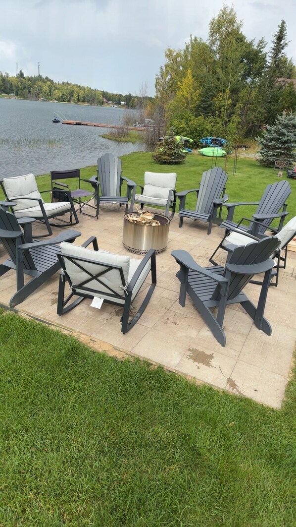 An outdoor seating area with Adirondack chairs and a fire pit, overlooking a lake. - Beautiful sunsets from the Lakeside Suite, deck on Longmere Lake, Soldotna AK (Soldotna)