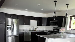 A modern kitchen with dark cabinets, stainless steel appliances, and a wooden floor.