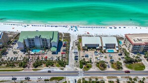 An aerial view of a coastal hotel with multiple buildings, a beach with umbrellas, and a parking lot.