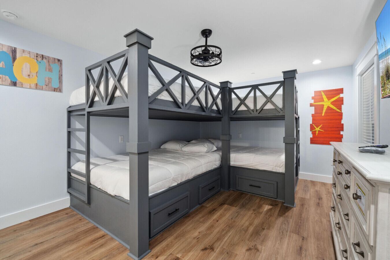 A bunk bed with a wooden frame and drawers, a ceiling fan, and a dresser with drawers.
