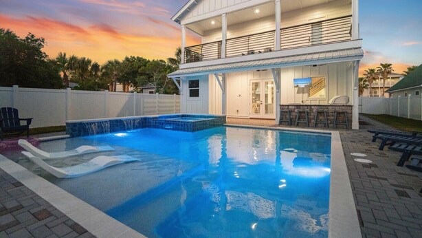 A two-story house with a swimming pool, a covered patio, and a view of the sunset.