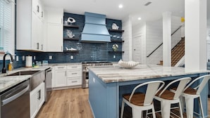 A modern kitchen with white cabinets, a blue backsplash, a central island with bar stools, and a stainless steel range hood.