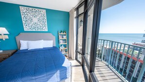 Un dormitorio con cama, estantería, un adorno en la pared y balcón con vista al océano.