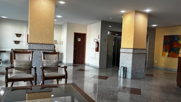 Um hall com mesa de vidro, cadeiras de madeira, um extintor de incêndio, uma porta e um refrigerador.