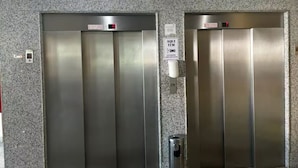 Duas portas de elevador com uma placa acima delas que diz 'AQUI TEM XOMO'.