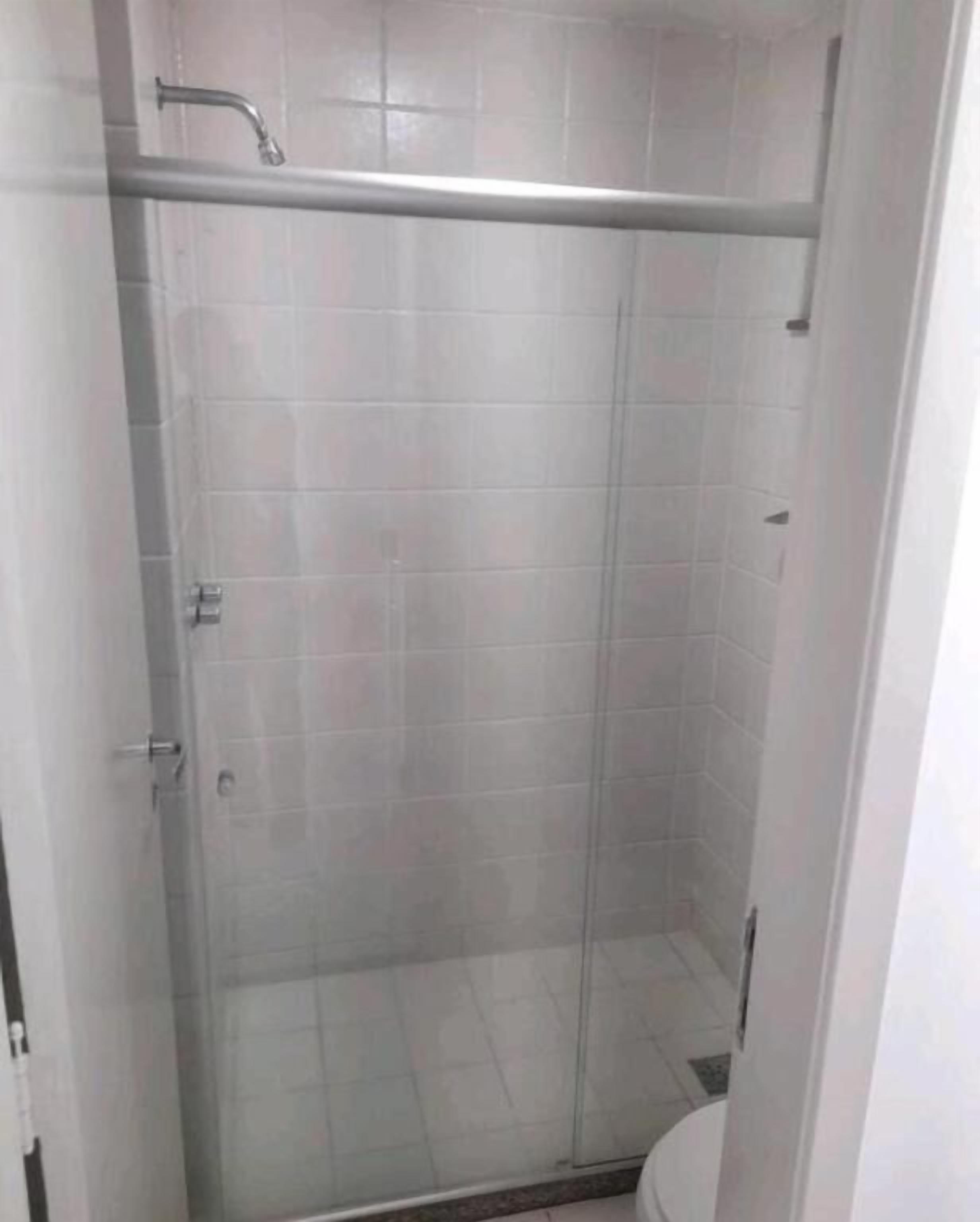 Une cabine de douche fermée par des parois en verre, dotée d’une poignée en métal et d’un sol carrelé.
