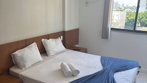 Quarto de hotel com uma cama grande, duas almofadas, um cobertor azul, um controle remoto e um ar condicionado.
