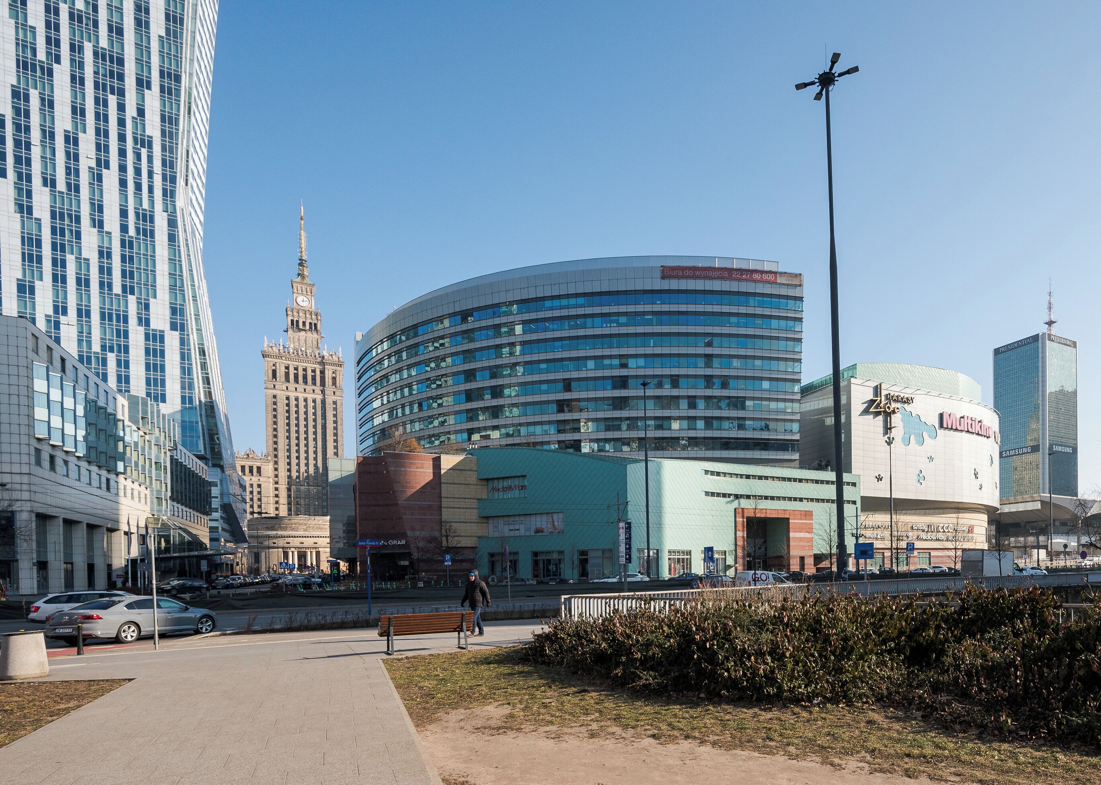 A cityscape with modern and historic buildings, a pedestrian walkway, and a person walking.