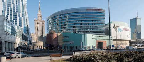 Un paisaje urbano con edificios modernos e históricos, un paseo peatonal y una persona caminando.