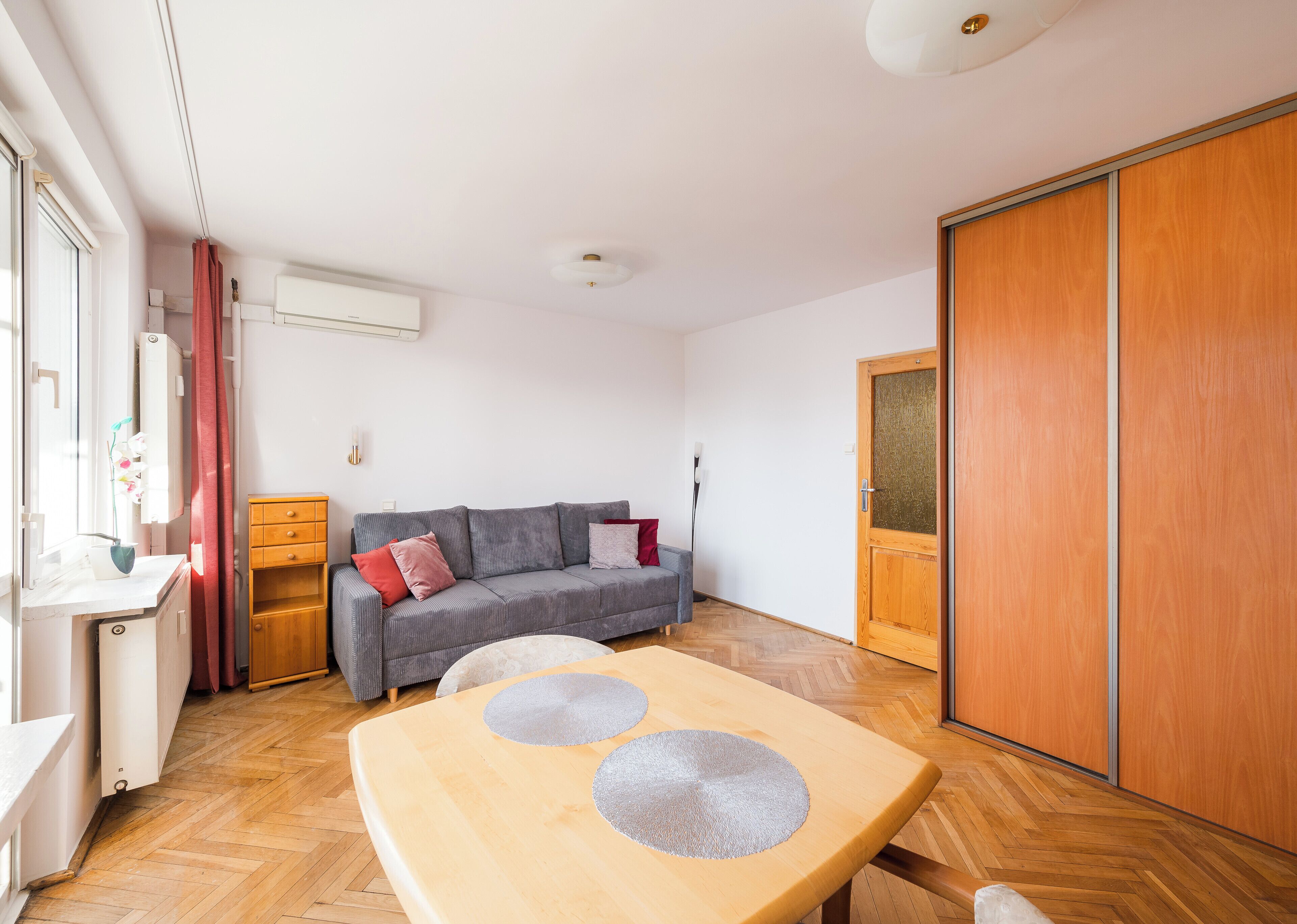 Una sala moderna con un sofá gris, una mesa de madera y un amplio armario.