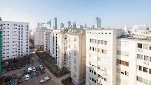 A high-rise residential building with multiple balconies, a parking lot with several cars, and a clear view of the city skyline in the background. - Złota Standard Studio (Warszawa)