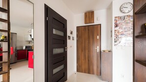 A hallway with a black door, a wooden door, and a wall with a clock and photos. - Marywilska 67 Inviting Apartment (Warszawa)
