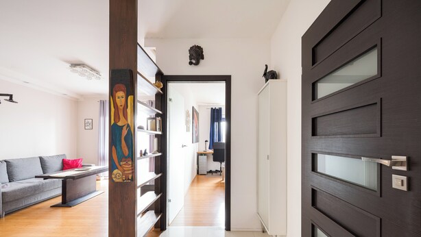 A modern living room with a grey sofa, wooden bookshelves, and a dark wooden door with glass panels. - Marywilska 67 Inviting Apartment (Warszawa)