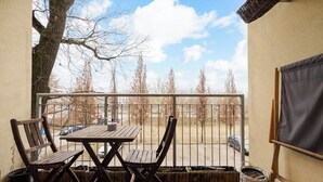 A balcony with a wooden table and chairs, a wicker basket, and a view of trees and a parking lot. - Marywilska 67 Inviting Apartment (Warszawa)