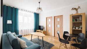Ein modernes Wohnzimmer mit Sofa, Couchtisch und Fernseher. Zwei Türen und ein Bücherregal sind ebenfalls vorhanden.