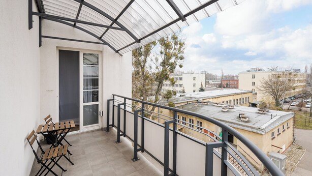 Ein Balkon mit Tisch und Stühlen, einer Glastür und Blick auf Gebäude und Bäume.