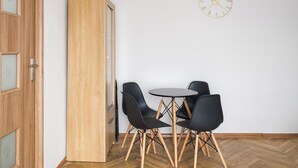 Ein Zimmer mit Holztür, einem hohen Schrank, einem runden Tisch mit vier Stühlen und einer Wanduhr.