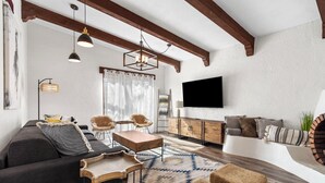 Un salon moderne avec un canapé, des fauteuils, une table basse, un téléviseur et un tapis à motifs.