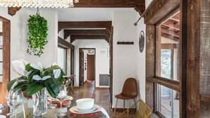 Un coin repas avec une table en verre, des assiettes blanches et un vase de fleurs. Il y a une chaise et une fenêtre donnant sur un beau paysage.
