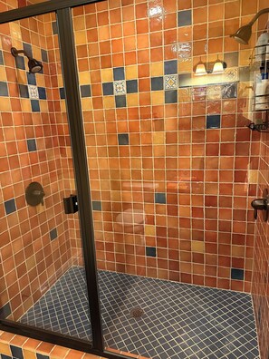 Un espace douche doté d’une porte en verre, de murs carrelés aux couleurs orange et bleue, et d’un pommeau de douche.