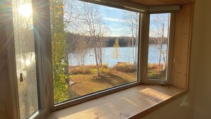 Een kamer met een groot raam met uitzicht op een meer en bomen.