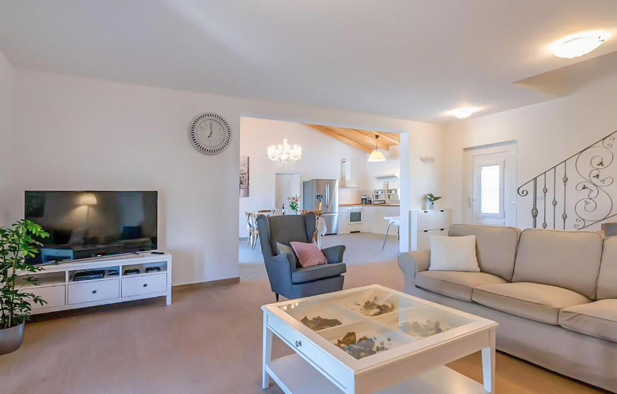 A modern living room with a flat-screen TV, a glass coffee table, a sofa, and a dining area with chairs.