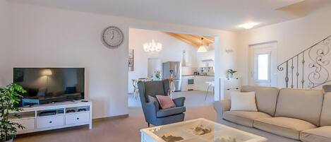 A modern living room with a flat-screen TV, a glass coffee table, a sofa, and a dining area with chairs.