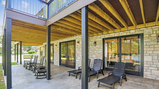 A covered outdoor seating area with stone walls and wooden beams, featuring multiple chairs and tables. - New Construction! 7 bedroom luxury lakefront  home in golf neighborhood! (Swanton)