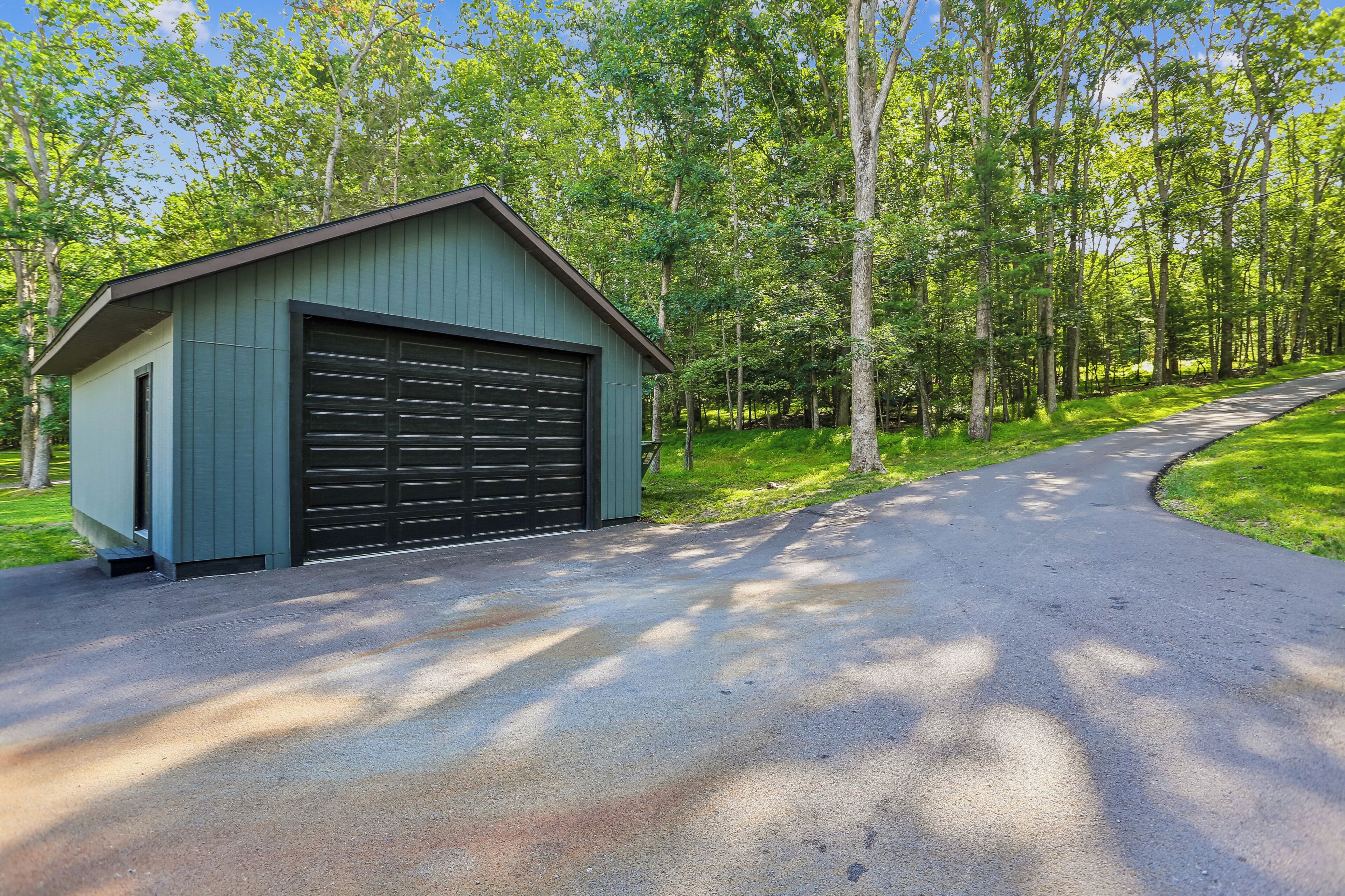 Ein eingeschossiges Gebäude mit einer Garagentür, umgeben von bewaldetem Gelände und einer gepflasterten Auffahrt.