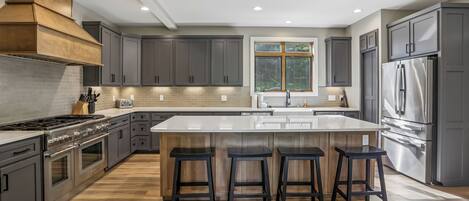 A modern kitchen with a central island, stainless steel appliances, and a large window.