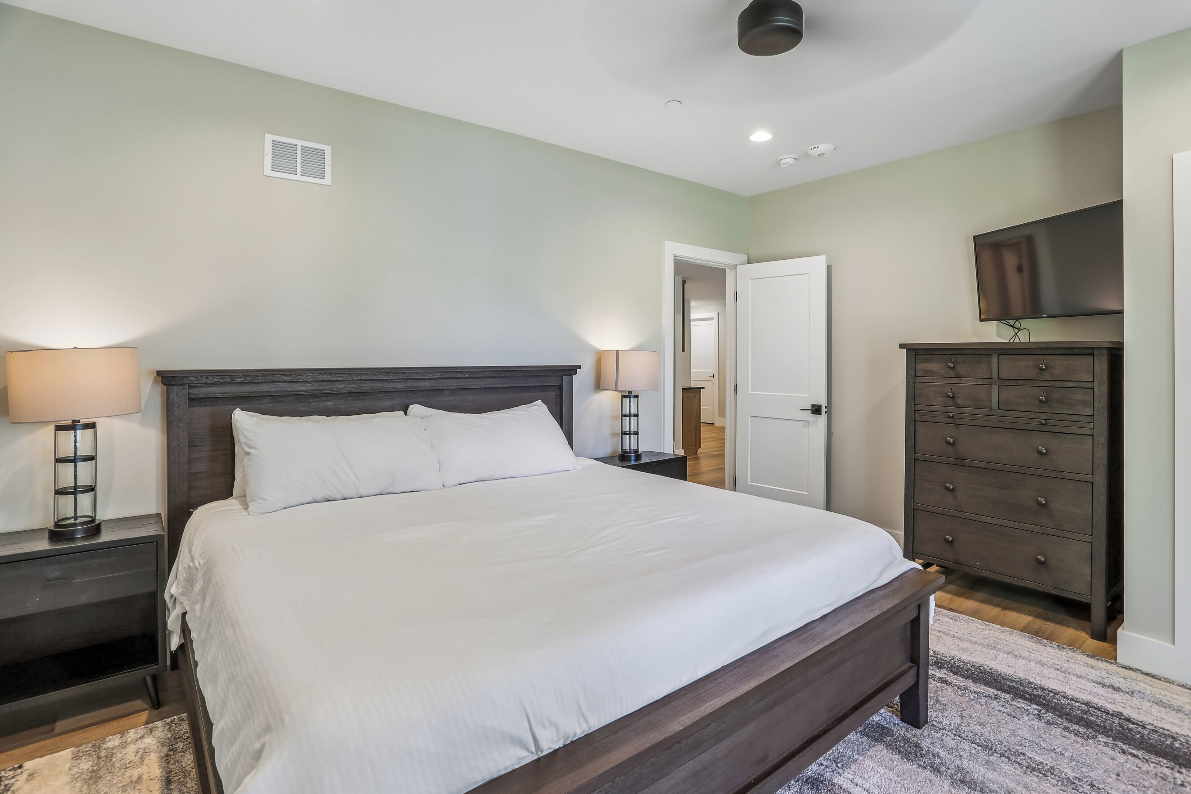 Une chambre à coucher avec un grand lit, des lampes de chevet, une commode et un téléviseur fixé au mur.