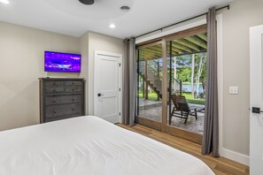 Een slaapkamer met een bed, een televisie aan de muur, een dressoir en een schuifdeur naar een buitenruimte met een trap en tuinmeubilair.