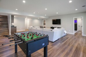 Un saló modern amb un taula de futbolí, un sofà, una televisió i una zona de cuina.