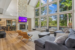 A spacious living room with a stone fireplace, large windows, and modern furniture. - New Construction! 7 bedroom luxury lakefront  home in golf neighborhood! (Swanton)