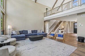 Un vaste espace de vie comprenant un canapé d’angle, une table basse et un plafond haut, avec accès à un balcon.