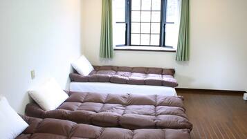 A room with a large bed, a window with curtains, and a wooden floor.
