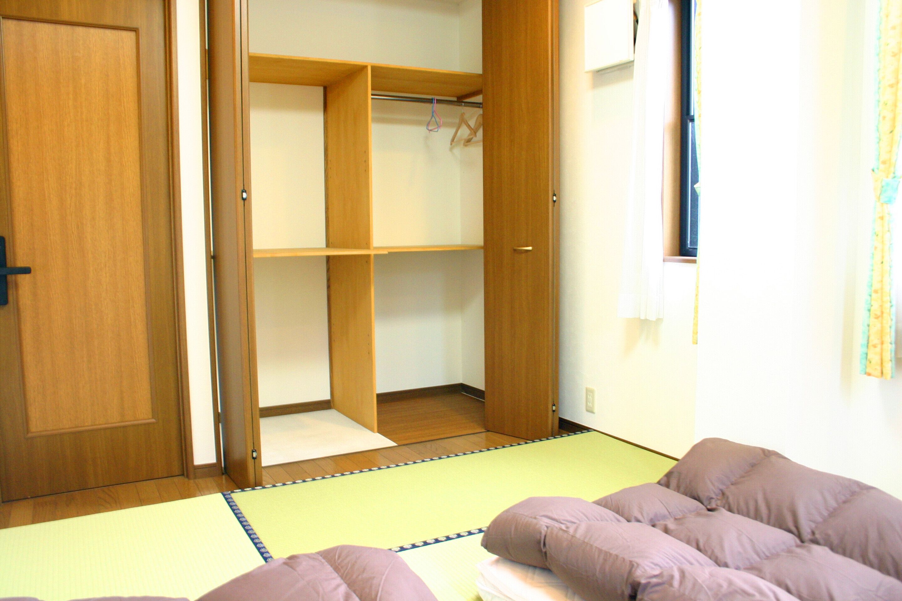 A room with a tatami mat floor, a wooden closet, and a bed with a purple blanket.