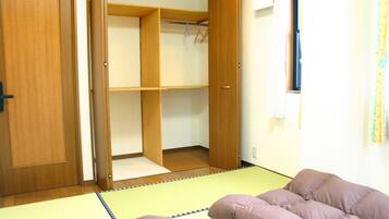A room with a tatami mat floor, a wooden closet, and a bed with a purple blanket.