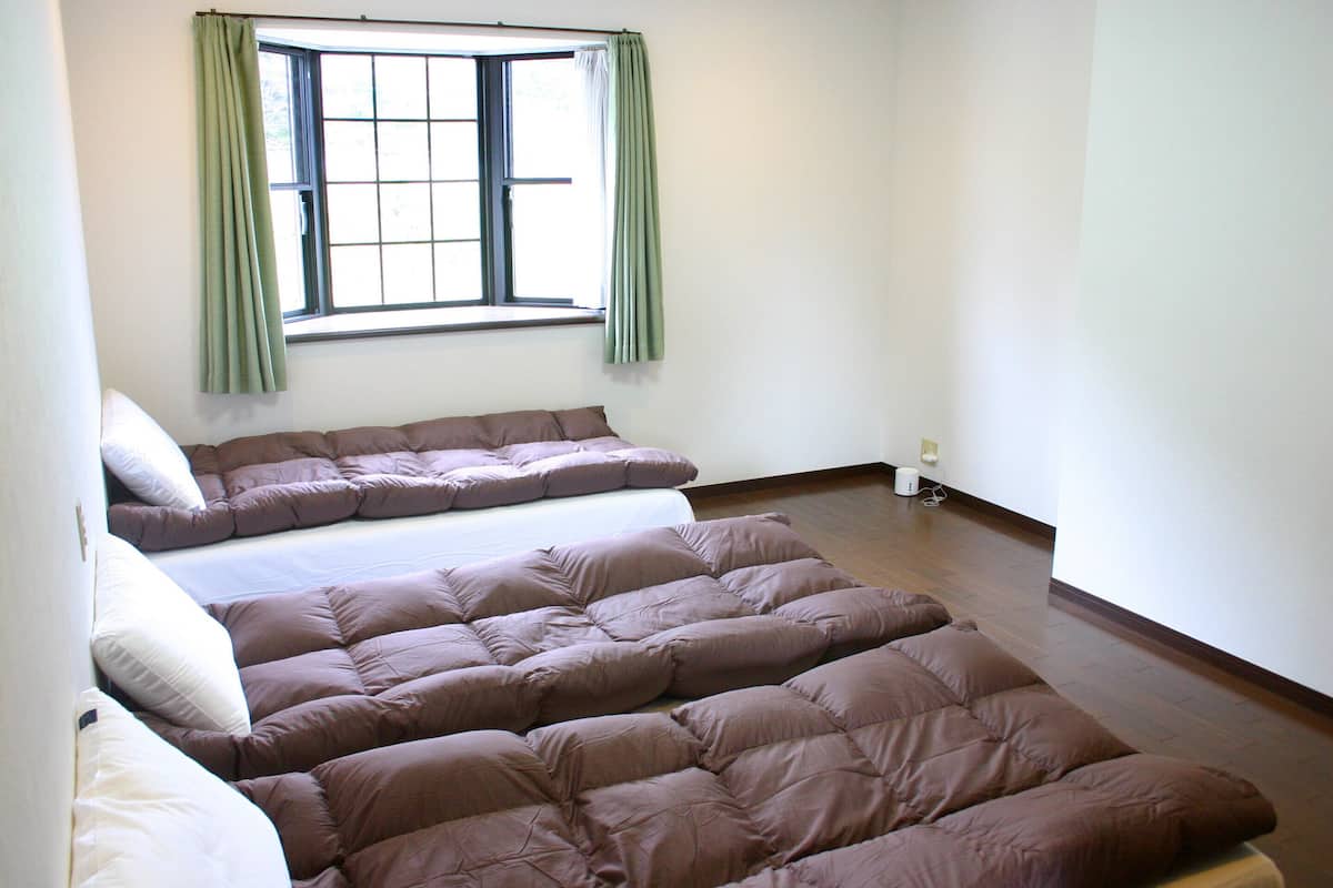 Quarto com cama grande, janela com cortinas e piso de madeira.