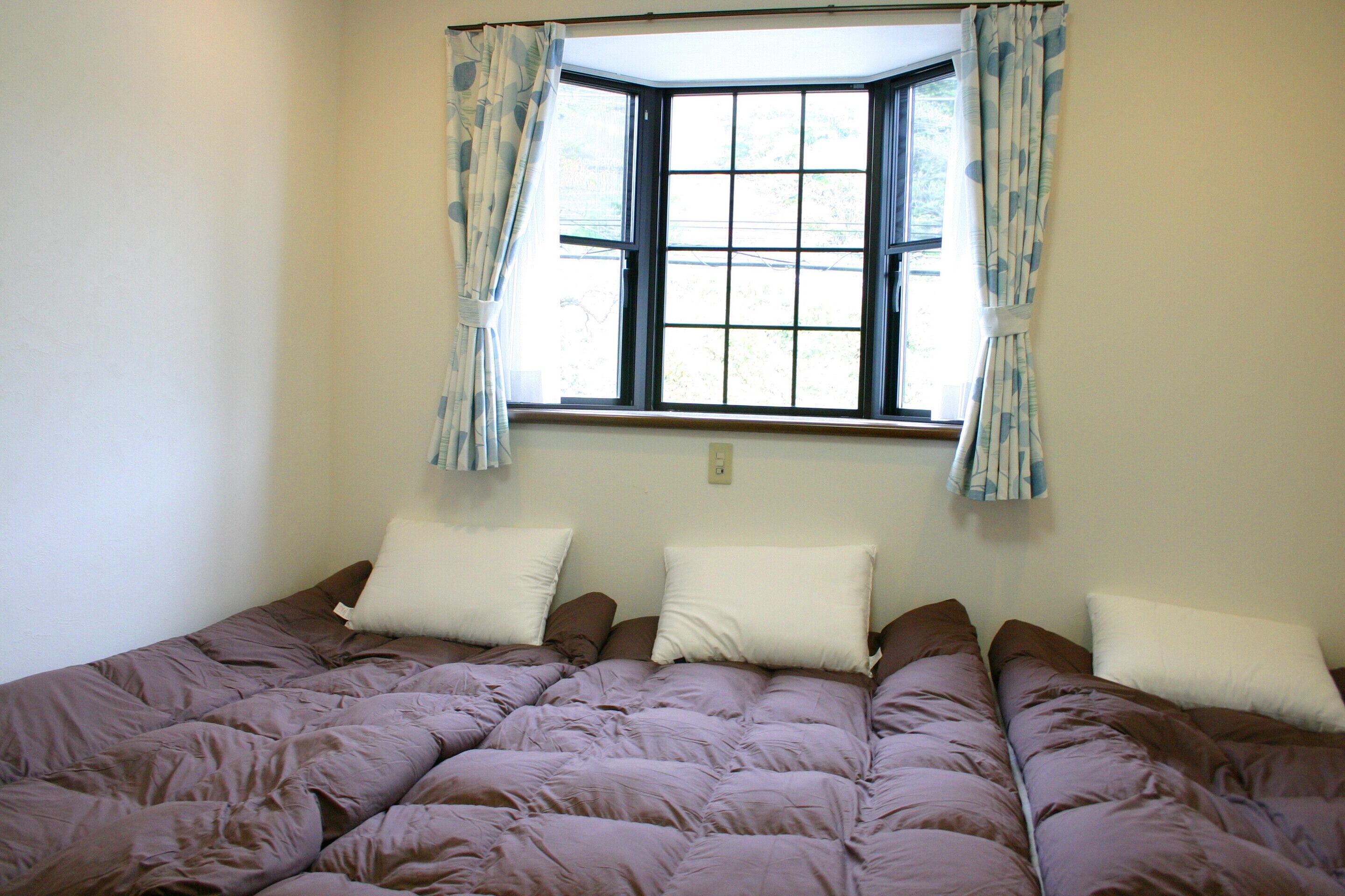 A bedroom with a large bed, a window with curtains, and a wall-mounted light switch.