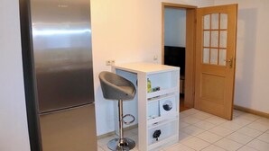 A compact kitchen with a stainless steel refrigerator, a white bar stool, and a wooden door. - Vacation apartment at Walberla (Kirchehrenbach)