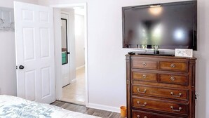 Ein Schlafzimmer mit einem Bett, einer hölzernen Kommode, einem Fernseher und einem Deckenventilator.