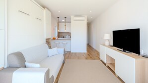 Una sala de estar moderna con un sofá, un televisor y una cocina al fondo.