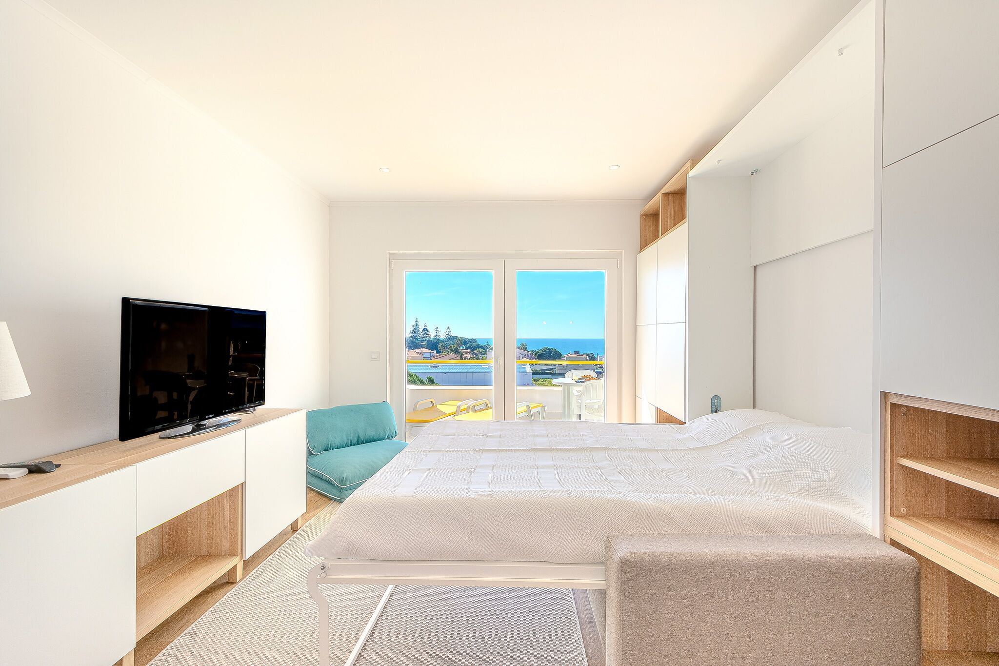 A modern bedroom with a large bed, a TV, and a balcony with a view.
